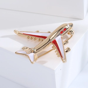 Close-up of a gold airplane brooch with red and white enamel details on a white base
