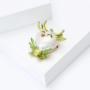Detailed macro shot of a white enamel owl brooch with golden antlers on a white pedestal