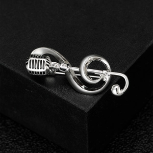 Close-up of a silver musical note and microphone brooch on a textured black display