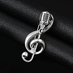Macro detail of silver G-clef and microphone brooch on black leather background