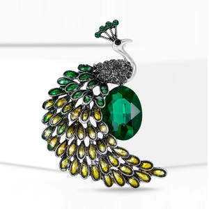 Détail d'une broche paon en argent avec cristaux verts et jaunes sur un fond blanc pur
