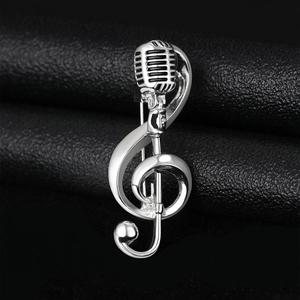 Detail view of silver treble clef and microphone brooch on black leather background