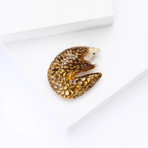 Macro detail of pangolin brooch with amber enamel scales on white geometric background