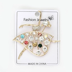 Dettaglio della spilla ballerina dorata con strass colorati su cartoncino da esposizione