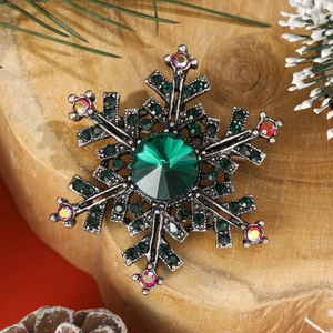 Sparkling snowflake brooch with green gemstone and rhinestones on wooden background