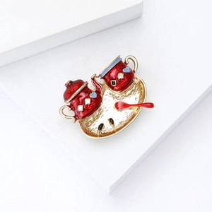 Detail of red enamel tea set brooch featuring a gold tray and intricate heart patterns