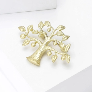 Gros plan d'une broche arbre en or mat avec détails de fruits ronds sur support blanc