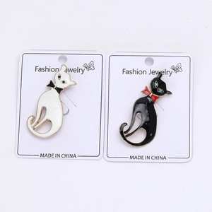 Détail des broches chat en émail noir et blanc avec yeux en cristal vert sur carte
