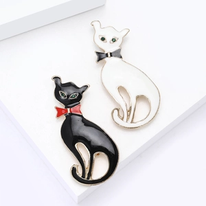 Ensemble de broches chats en émail noir et blanc avec yeux en strass verts sur fond blanc
