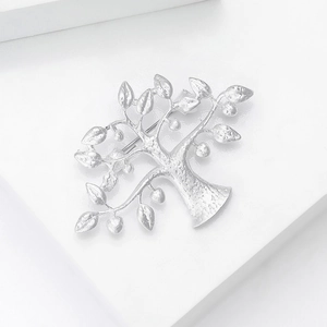 Détail macro d'une broche arbre de vie argentée mate sur fond géométrique blanc épuré