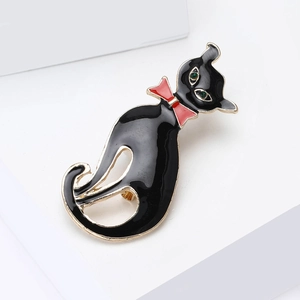 Détail d'une broche chat en émail noir avec nœud papillon rouge et yeux en pierre verte