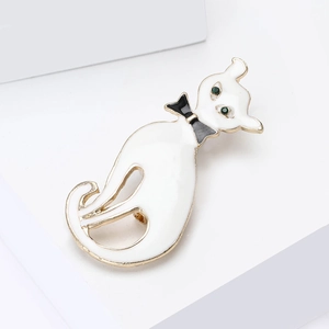 Détail de la broche chat en émail blanc avec bords dorés et yeux en gemme verte
