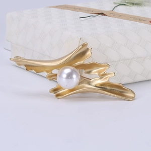 Détail d'une broche ondulée dorée mate avec une grande perle blanche élégante