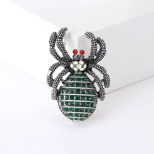 Vintage punk spider brooch with green rhinestones on minimalist white block background