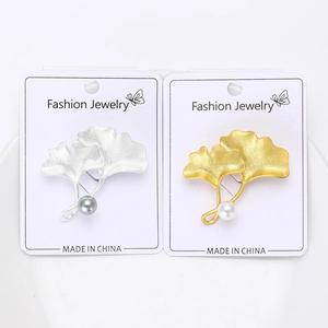 Détail de broches feuilles de ginkgo dorées et argentées avec perles sur carte