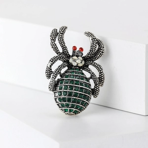 Macro shot of vintage silver spider brooch with green rhinestones on white blocks
