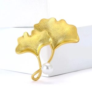 Élégante broche feuille de ginkgo dorée avec perle blanche sur fond blanc pur