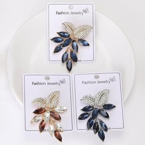 Three crystal leaf brooches in navy, brown, and clear stones on elegant white cards