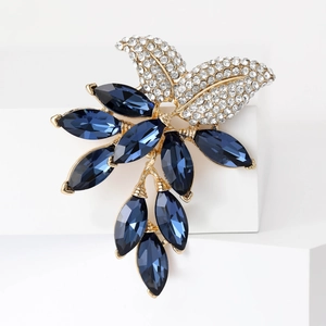 Detail of leaf brooch with gold base, white rhinestones, and navy blue crystals