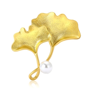 Élégante broche en feuille de ginkgo dorée avec perle blanche sur fond blanc pur