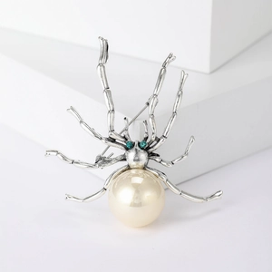 Vintage-Spinne-Brosche mit großer weißer Perle und grünen Kristallaugen auf Weiß