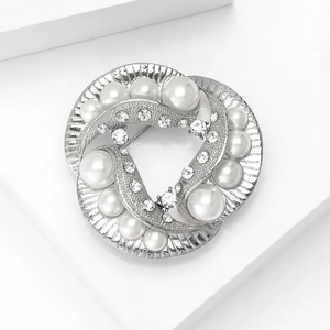 Detailed view of silver brooch with pearls and crystals on a white geometric stand