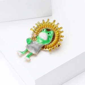 Détail d'une broche grenouille en émail vert avec un fond d'engrenage doré rayonné