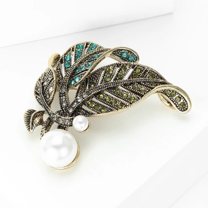 Eleganter Vintage Blatt-Brosche in Gold mit grünen Steinen und Perlen auf weißem Sockel