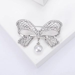 Broche nœud élégante en argent avec cristaux scintillants et perle sur un socle blanc
