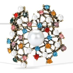 Vintage gold brooch with large pearl centerpiece and colorful rhinestones on white backdrop