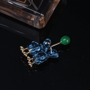 Detailed close-up of a blue enamel couple ducks brooch with a green bead on black surface