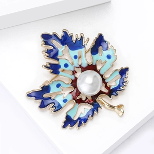 Détail macro d'une broche en forme de feuille émaillée bleue et rouge avec perle centrale