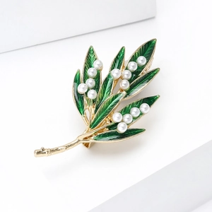 Close-up of golden metal brooch with green enamel leaves and delicate white pearls