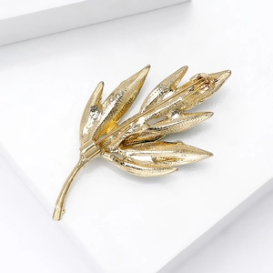 Golden leaf brooch featuring detailed texture and secure back pin on a white display