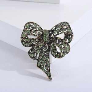 Macro detail of vintage bronze bow brooch with deep green rhinestones on white stands