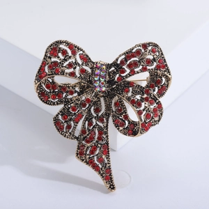 Vintage gold bow brooch with red rhinestones and iridescent crystals on white platform