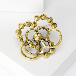Back view of a gold vintage woven brooch with a safety pin and central pearl accent