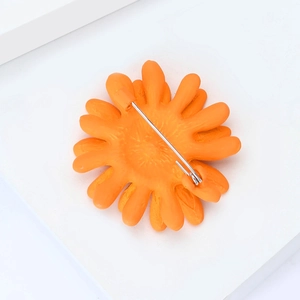 Vue macro de la broche marguerite orange montrant l'épingle de sûreté en métal au dos