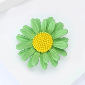 Macro d'une broche marguerite verte avec centre jaune texturé et pétales en résine