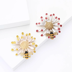 Enamel daisy and bee brooch set with red and yellow petals on white background