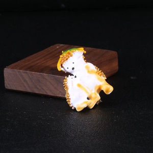 Detailed close-up of a white enamel hedgehog brooch with bright orange and green accents