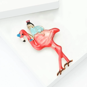 Broche de esmalte con flamenco rosa y niña en vestido azul sobre soporte blanco