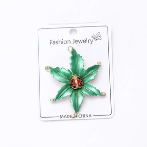 Close-up of alloy enamel ladybug on green leaf brooch pinned on a white display card