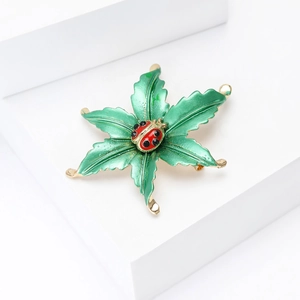 Enamel ladybug on green leaf brooch with gold metal edge on white platform