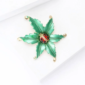 Green enamel leaf brooch with a red ladybug on a minimalist white geometric background