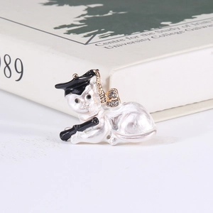 Detailed close-up of a pearly white cat brooch with black graduation hat and golden bow