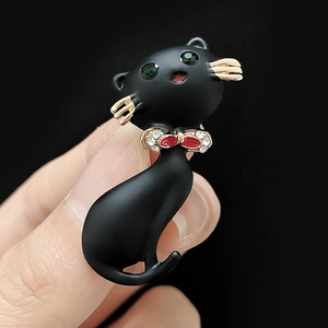 Détail d'une broche chat noir avec yeux en gemme verte et nœud papillon scintillant