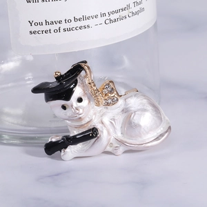 Macro shot of a cute white graduate cat brooch with a black cap and rhinestone bow