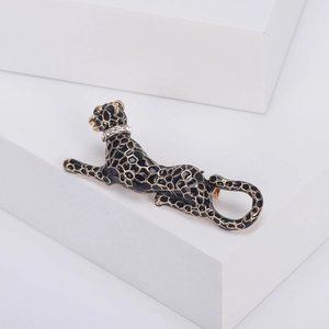 Elegant leopard brooch with black enamel spots and green gemstone eyes on white stand