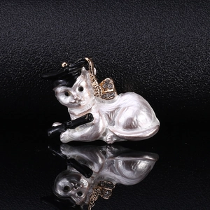 Close-up of white enamel graduation cat brooch with rhinestones and its mirror reflection